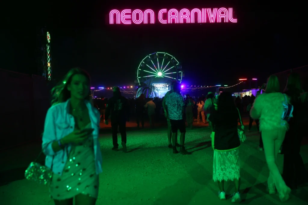 festival goer walks by the neon carnival sign