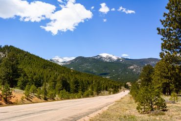 a view of snow-capped mountains and coniferous forest from a road in Estes Park, Colorado
