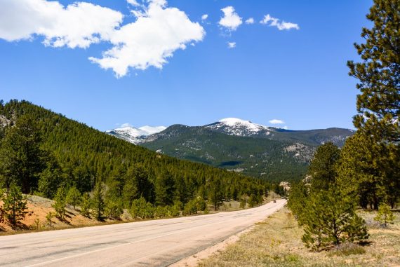 a view of snow-capped mountains and coniferous forest from a road in Estes Park, Colorado